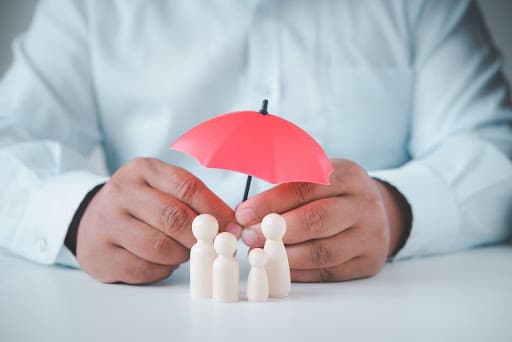 Businessman holding tiny umbrella over a wooden model family