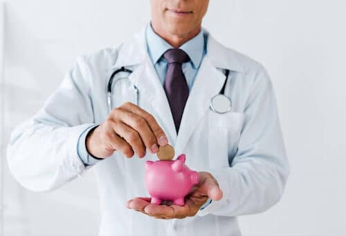 Doctor in a white coat putting a coin in a piggybank