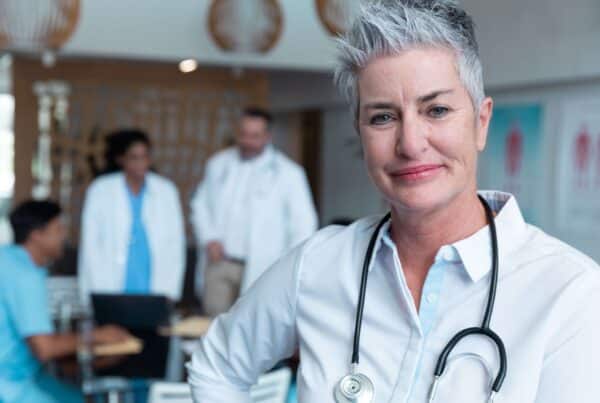 Older female caucasian doctor with stethoscope in foreground, other medical professionals blurry in background