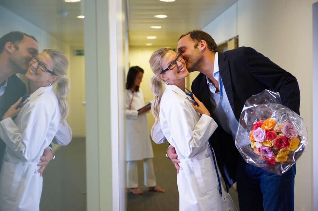 Man in a suit holding flowers and hugging a woman doctor