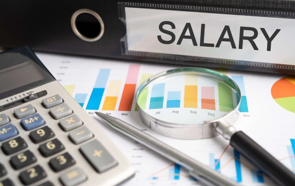 salary binder, magnifying glass, pen, and calculator sitting on top of paperwork